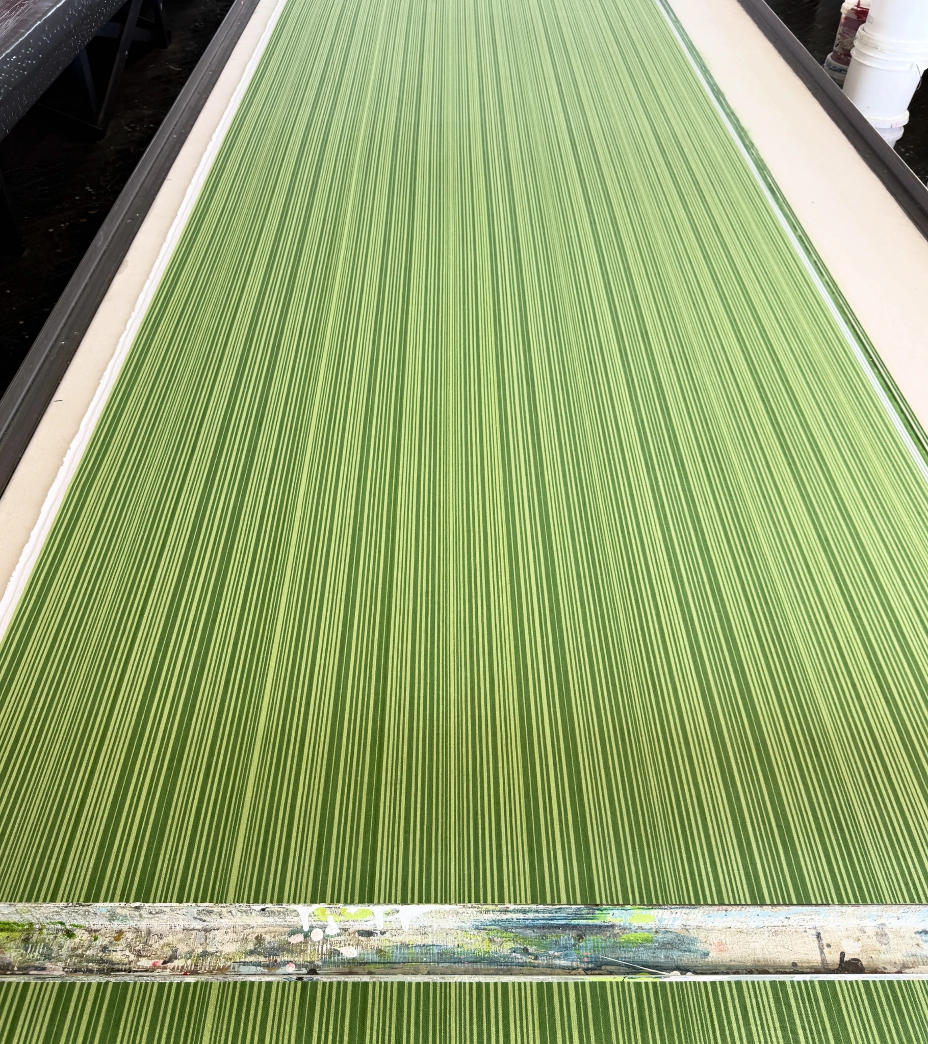 A close-up view of bright green and white vertically striped fabric stretched out flat on a long printing table.